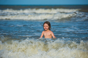 Kid playing on the beach on summer holidays. Kid swimming in sea with wawes.