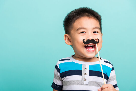 Funny Happy Hipster Kid Holding Black Mustache Props For The Photo Booth Close Face, Studio Shot Isolated On A Blue Background, Men Health Awareness, Prostate Cancer Awareness