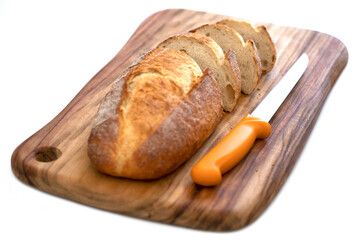 Fresh daily baking healthy plain sourdough loaf placing on top of cutting wooden board with a sharp knife sliding into small pieces  isolated white background 