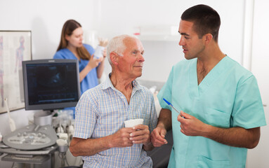 Man doctor and elderly man patient before ultrasound diagnostic, woman on background