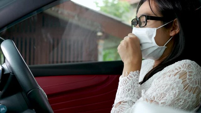 Sick woman in a protective mask have flu symptoms coughs and closes mouth with her hands in a car. Health care and medical concepts.