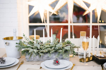 Beautifully set table with decorations, candles and lanterns. The living room is decorated with garlands and a Christmas tree. Festive atmosphere