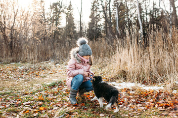 Girl in a gray hat and a warm jacket with a puppy dogs walk in the autumn forest, trees and grass
