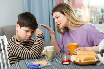 Upset mother and unhappy son arguing during breakfast in domestic interior