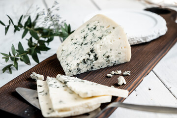 a piece of dor blue cheese on a cheese board with knives. delicacy blue cheeses. Homemade cheese...
