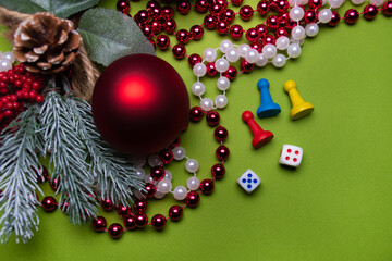 Single red New Year ball on red and white beads with a Christmas tree branch and red berries on a green background with three game chips of different colors: red, blue and yellow, Christmas background