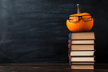 Teacher's table, pumpkin with glasses, on chalkboard background. Template concept of autumn mood, halloween and Thanksgiving. Copy space.