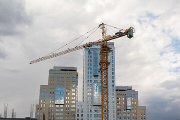 Fototapeta premium tower crane builds a high-rise house with a monolithic house against the background of skyscrapers of business centers