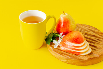 Cup of pear juice and ripe pears on wooden cutting board and yellow background with copy space.