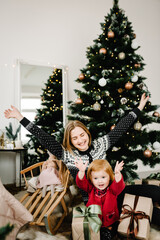 Mother exchanging gifts with daughter. Parent and little child having fun near Christmas tree indoors. Loving family with presents in room. The morning before Xmas. Portrait mom and child close up.