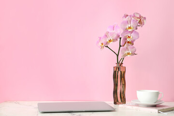 Vase with beautiful orchid flowers, laptop and cup of coffee on table