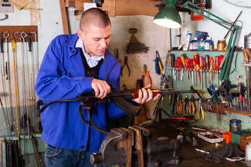 Professional gun repairman performing assembly of Kalashnikov rifle after repair or preventive maintenance in workshop.