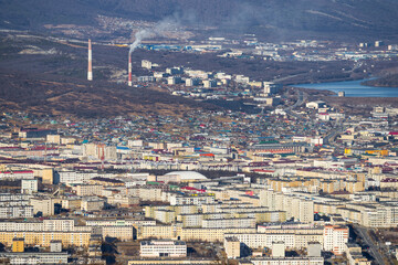 Aerial view of the city of Magadan. Top view of the streets and buildings. In the distance, the smoking chimneys of a thermal power plant. Magadan, Magadan region, Siberia, Far East of Russia.