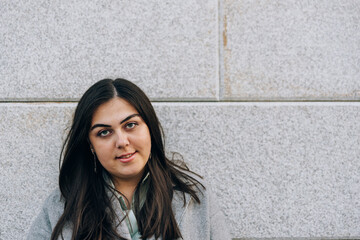 Portrait of a beautiful young adult girl against a gray wall