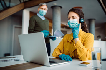 Smiling businesswoman with face mask making video call over laptop while working in the office.