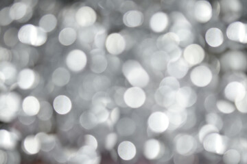 Silvery bokeh background. Texture with shining blurred lights of silver colors. Abstract Christmas festive background. Blurry white lights.