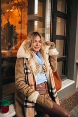 Portrait of pretty blonde girl walking in city drinking coffee