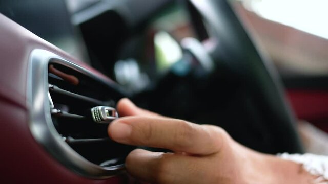 Close-up of a woman's hand adjusting the ventilation grill on the console inside the car.