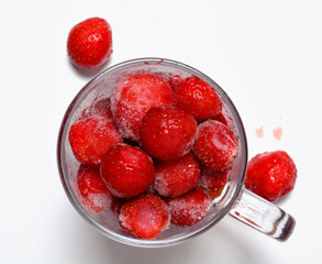 freshly frozen strawberries in a glass mug on a white background.