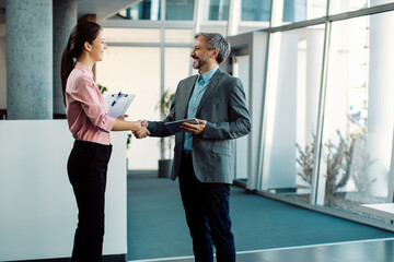 Happy business colleagues handshaking while greeting in a lobby of an office building. © Drazen