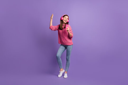 Full length body size photo of girl in headphones singing keeping smartphone like microphone isolated on bright purple color background