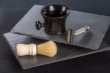 Shaving kit of metallic safety razor with blades and soft shaving brush with bowl on dark background 