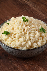 Cooked rice in a bowl, close-up on a wooden table, served with parsley leaves