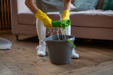 A woman in rubber gloves wrung out a green rag. Professional cleaning service. Cleaning floors with a mop. Squeezing, twisted rag. Housekeeping - obrazy, fototapety, plakaty