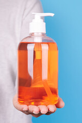Hand with orange soap bottle on blue background.