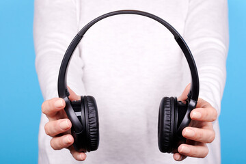 Hand with black wireless headphones on blue background.