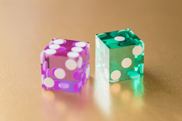 Two glass dice, green and pink, on a gold background in sunlight. Result six and one. Selective focus macro photography.