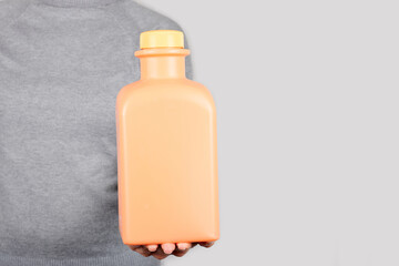Hand with orange juice in bottle on grey background.