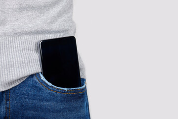 Mobile phone in jeans pocket on grey background.