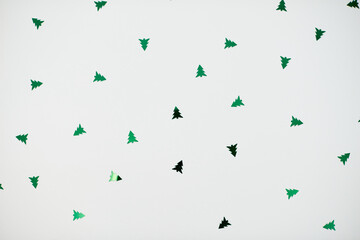 Festive background. Sparkling green confetti in shape of tree on white background. Christmas, Happy New Year Day, holiday concept. Flat lay, top view, copy space..