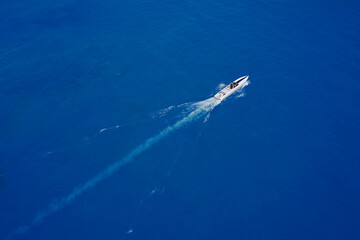 Speed boat of white color fast motion on blue water in the rays of the sun top view. Speed boat at sea, view from above.