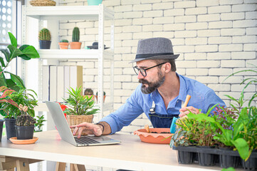 Relax hobbies lifestyle of Caucasian male  wearing apron using a laptop to learning to planting in the indoor garden room at home.