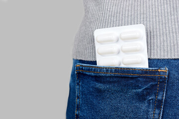 Medical pills in jeans pocket on grey background.
