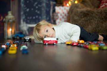 Cute toddler boy, sitting around many car toys on the floor, playing