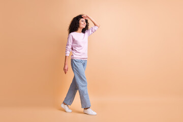 Fototapeta na wymiar Full size photo of optimistic go curly girl see someone wear sweater jeans sneakers isolated on peach color background