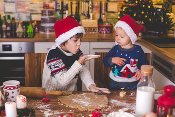 Sweet toddler child and his older brother, boys, helping mommy preparing Christmas cookies at home