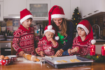 Sweet toddler child and his older brother, boys, helping mommy preparing Christmas cookies at home .