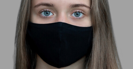 Portrait of a young European girl with long hair in a black medical mask on a gray background. Face masks have become the new norm of life.