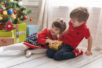 Boy gives a Christmas present to a girl in a bright sunny room