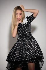 Fototapeta premium beautiful girl blonde teenager in a stylish black dress dress with white polka dots posing in the studio