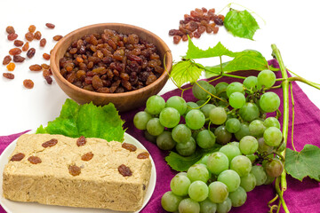 Yellow raisins, bunch of grape with leaves and halva on table cloth. Organic food and drinks concept