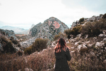 A girl from behind in the middle of nature looking at the mountain.