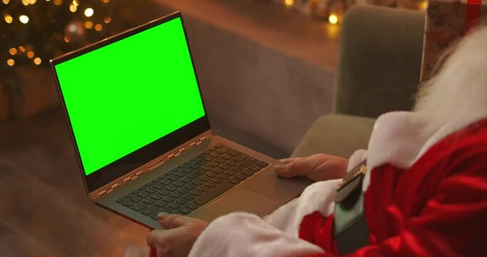 During the quarantine, Santa Claus congratulates the children using a video link. Green screen of the laptop on the lap of Santa Claus. Back view of a laptop screen with a chromakey on the background