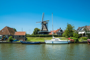 Fototapeta na wymiar Alte Windmühle und Boote am Kanal, Fluss, Wasser in Holland mit blauer Himmel ohne Wolken