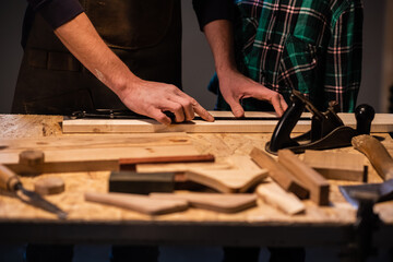 close-up of the work of a man and a boy at a carpenter's table, on the table are a plane, chisel, Board, workbench, ruler and other items