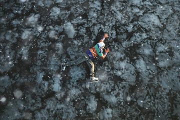 Fototapeta na wymiar a man in ice skates lies on the transparent ice of the lake, view from above, aerial photography